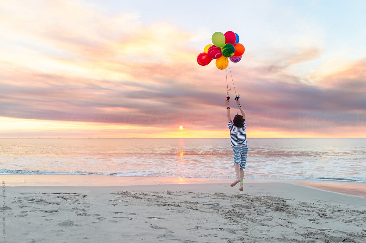 Boy aloft with balloons at the beach at sunset