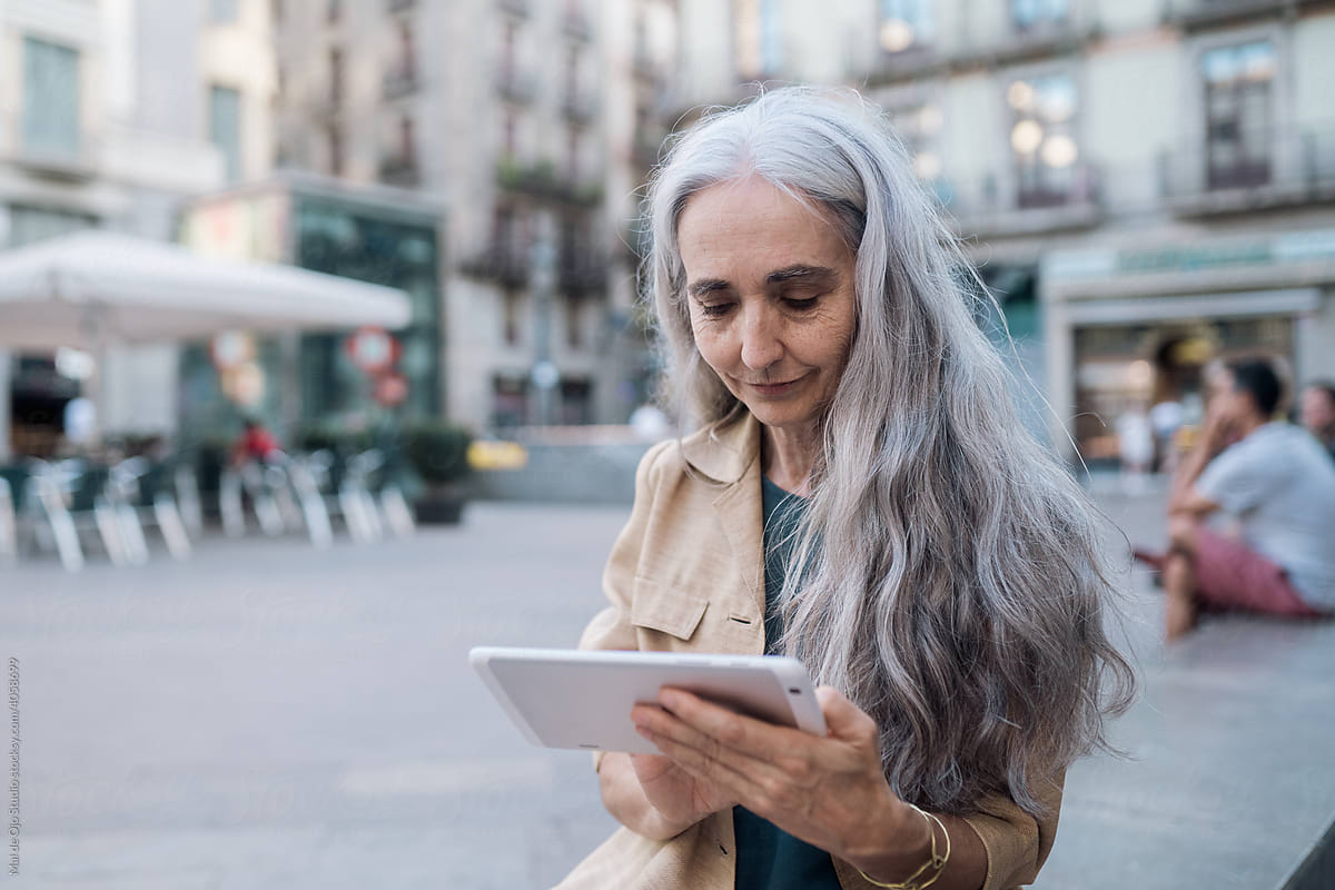 Grey-haired woman  sitting in the street using a tablet
