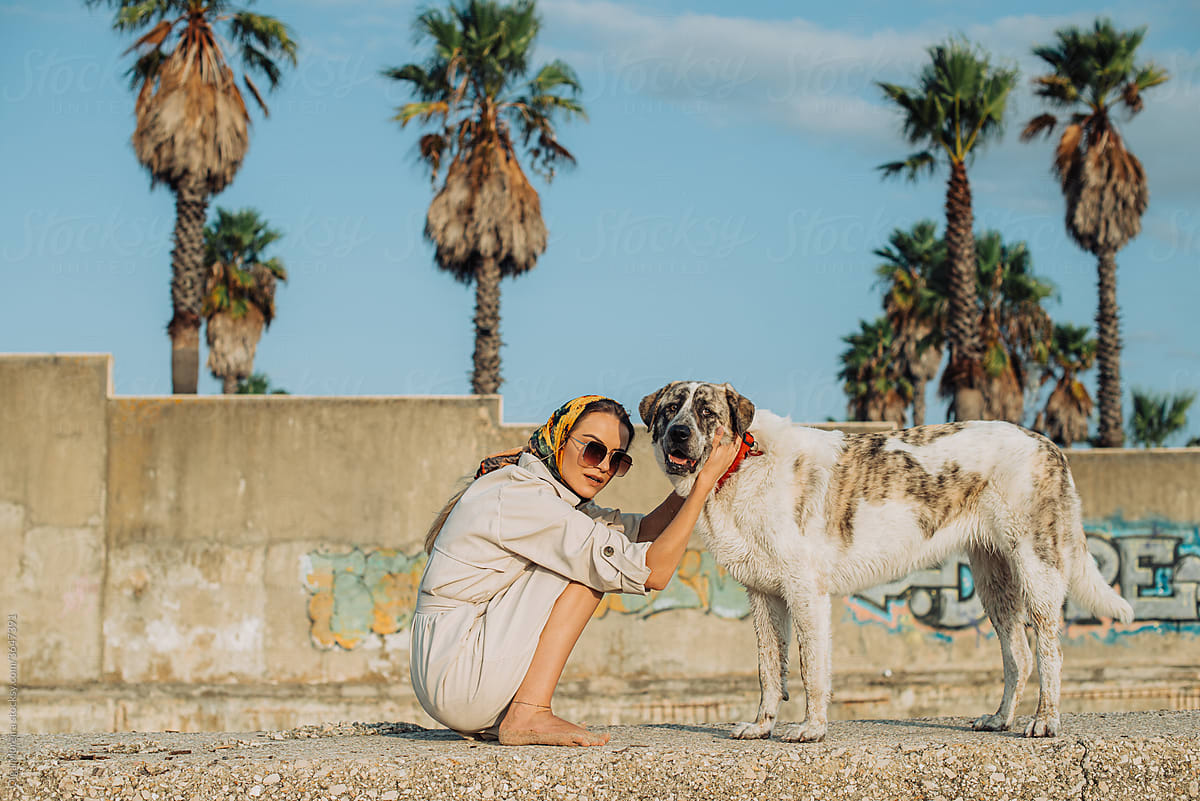 Woman and her dog with a wall and palm trees on background