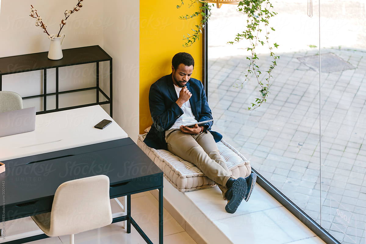 Resting black man on window sill with gadget in office
