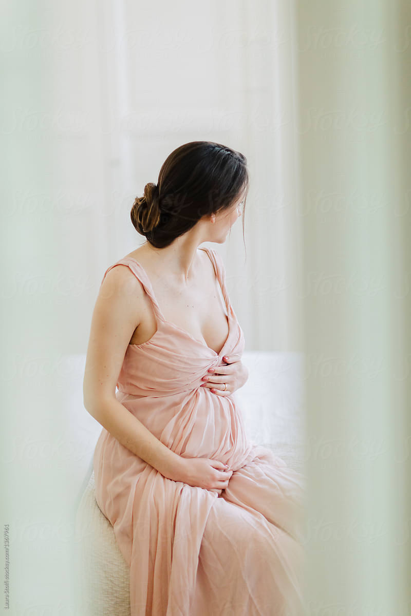 Intimate portrait through open doors of beautfiul mother-to-be sitting on her bed