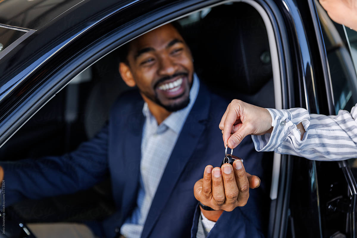 Happy man taking new car keys from sales executive at dealership