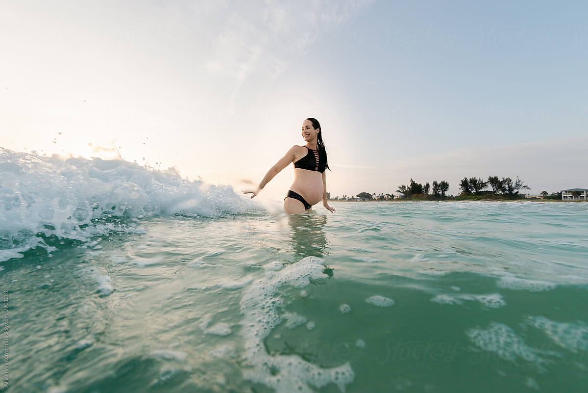 A pregnant mom in bikini waits for a wave
