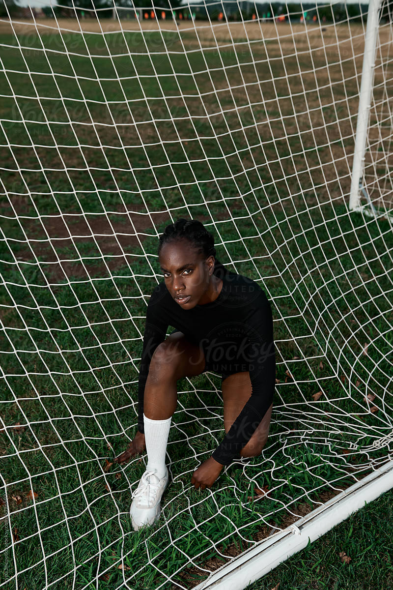 African American female sitting in soccer goal On Field