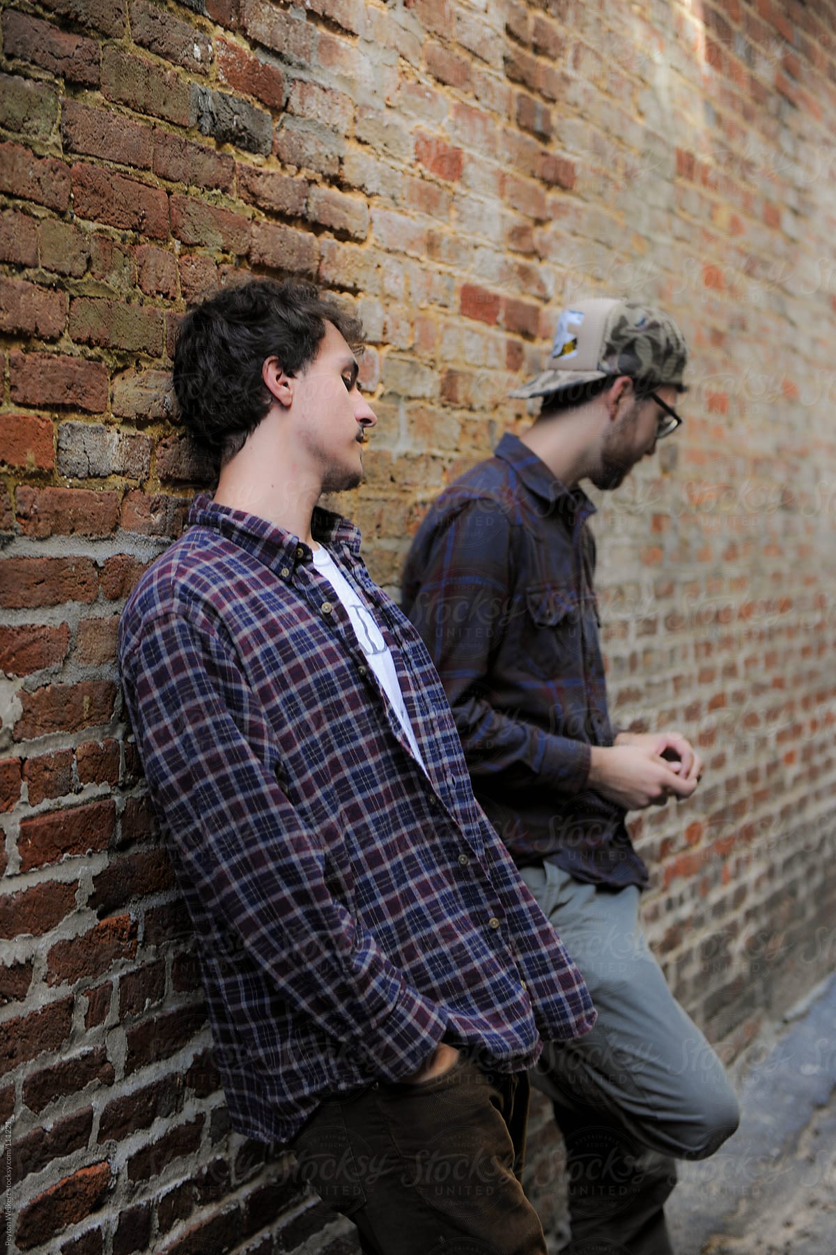 Hip young men hanging out and relaxing against a brick wall in an alley way