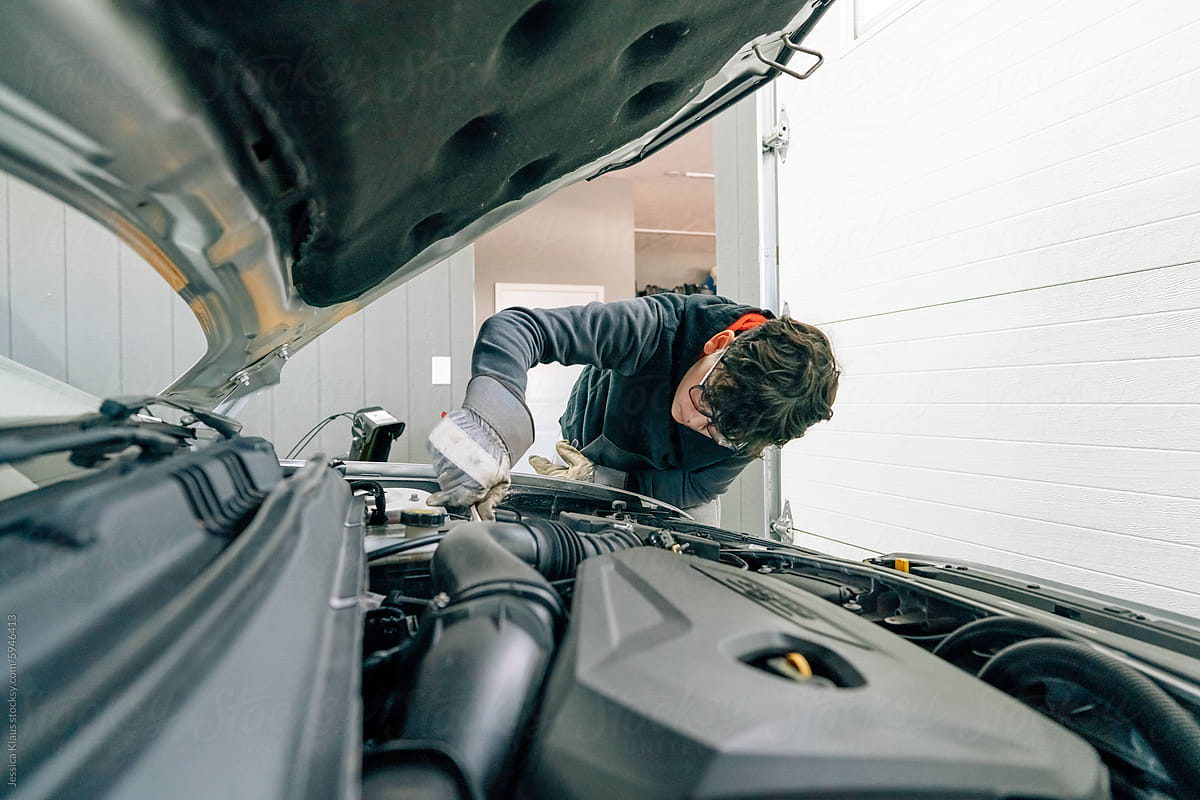 Teen boy doing maintenance on the engine of a car.