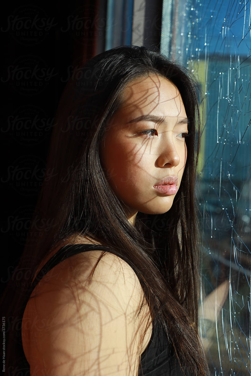 young Asian female  behind broken glass window