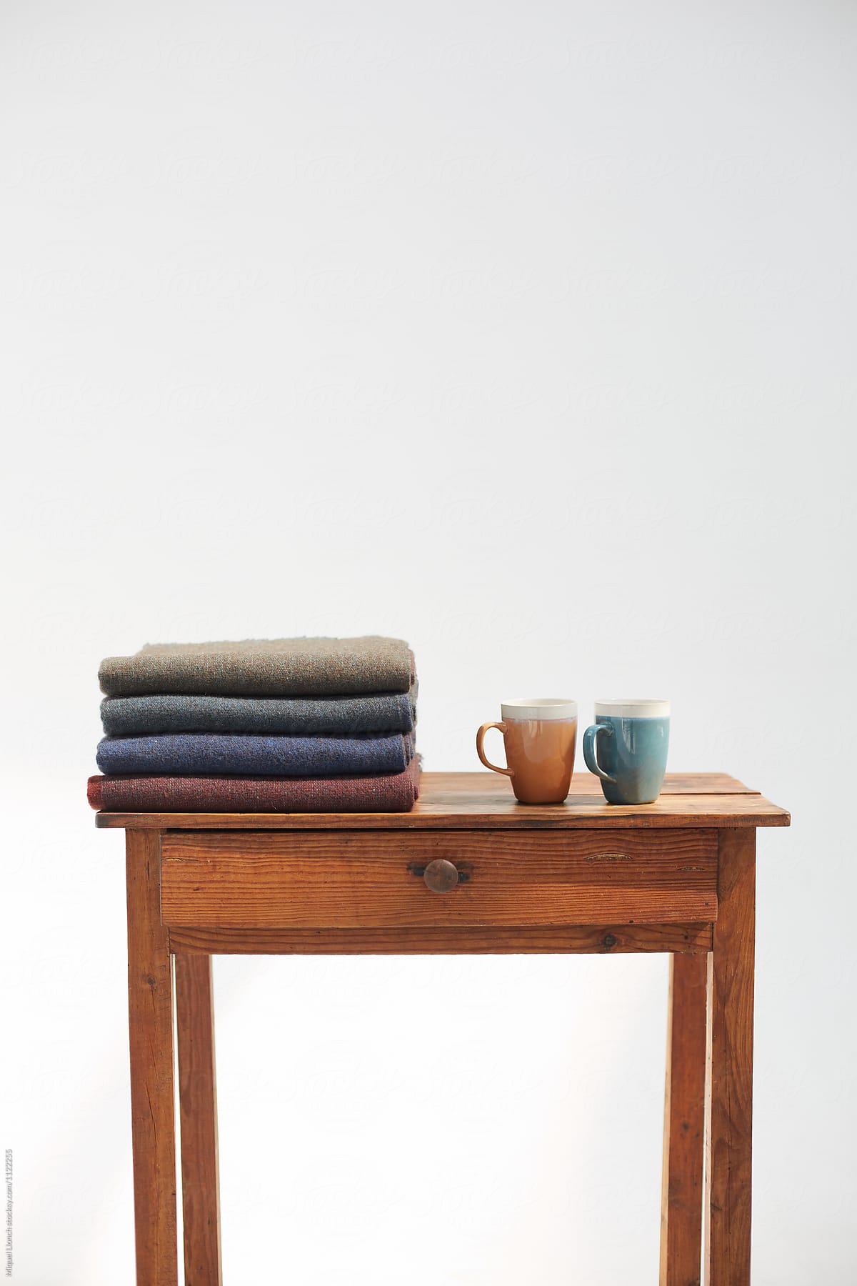 Stack of wool blankets and two ceramic mugs on a wooden table