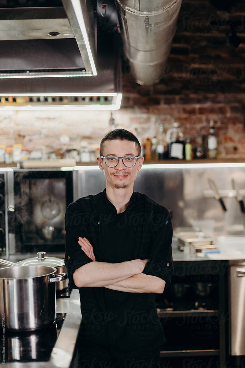 Smiling chef in black uniform standing in modern kitchen