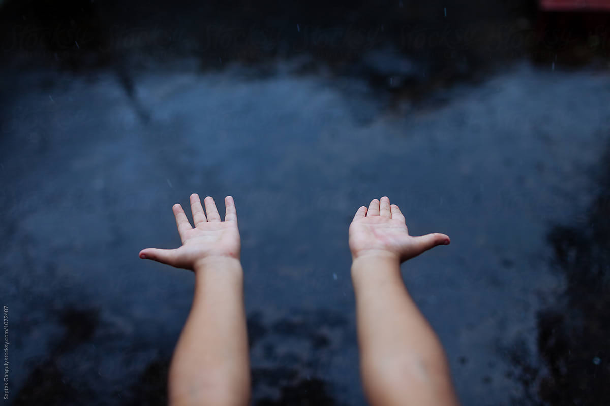 Child extending her hands out in the rain,top view