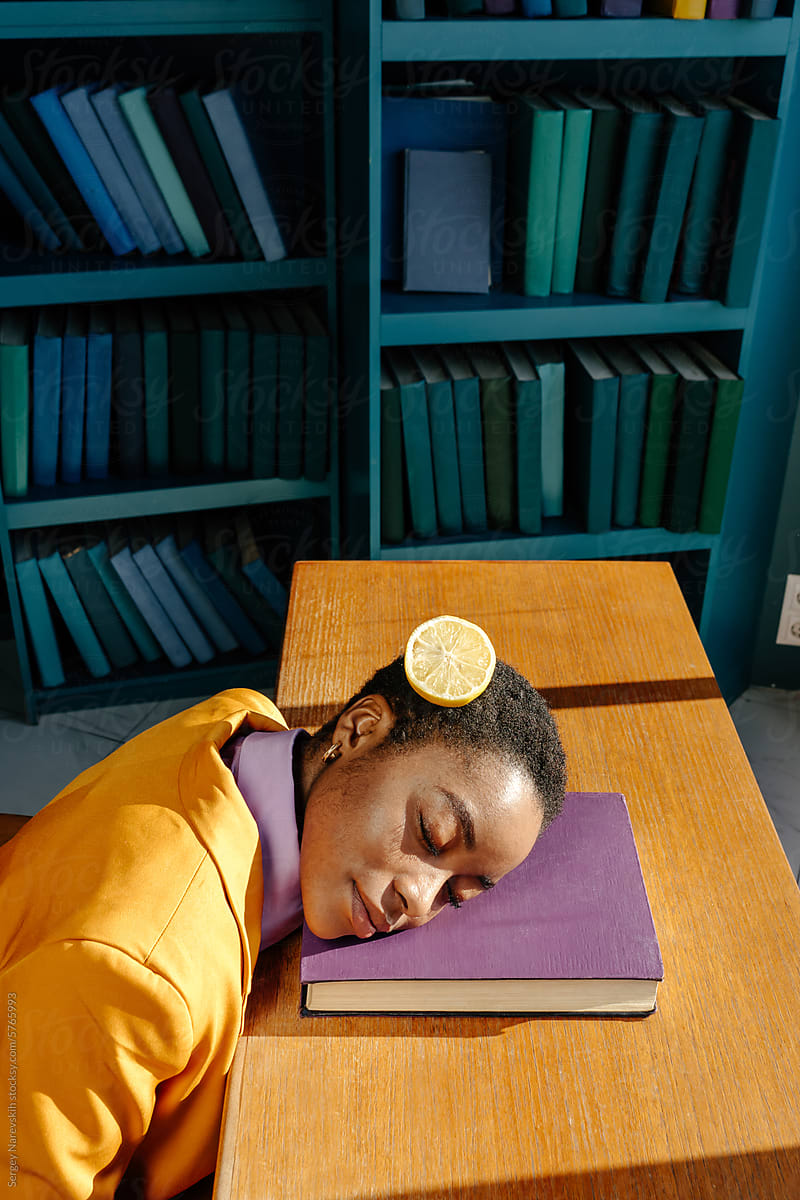 Woman with closed eyes lying on book, cutted lemon on hair