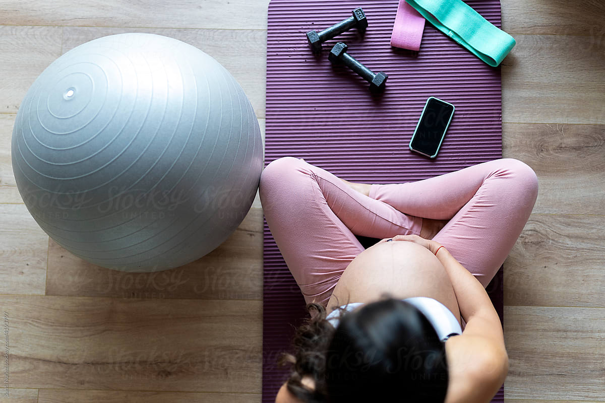 Pregnant woman using cell phone exercising at home.