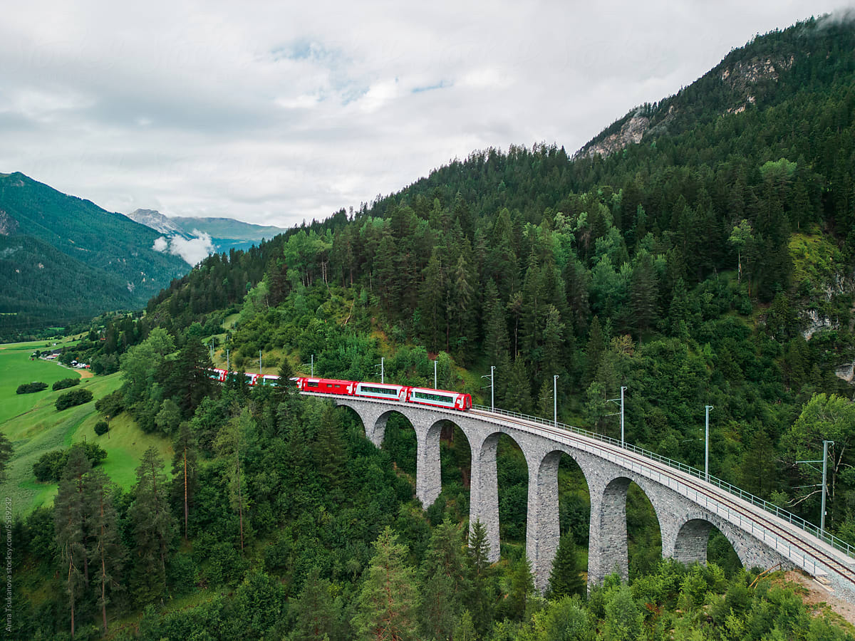 Red train passing viaduct in Swiss Alps
