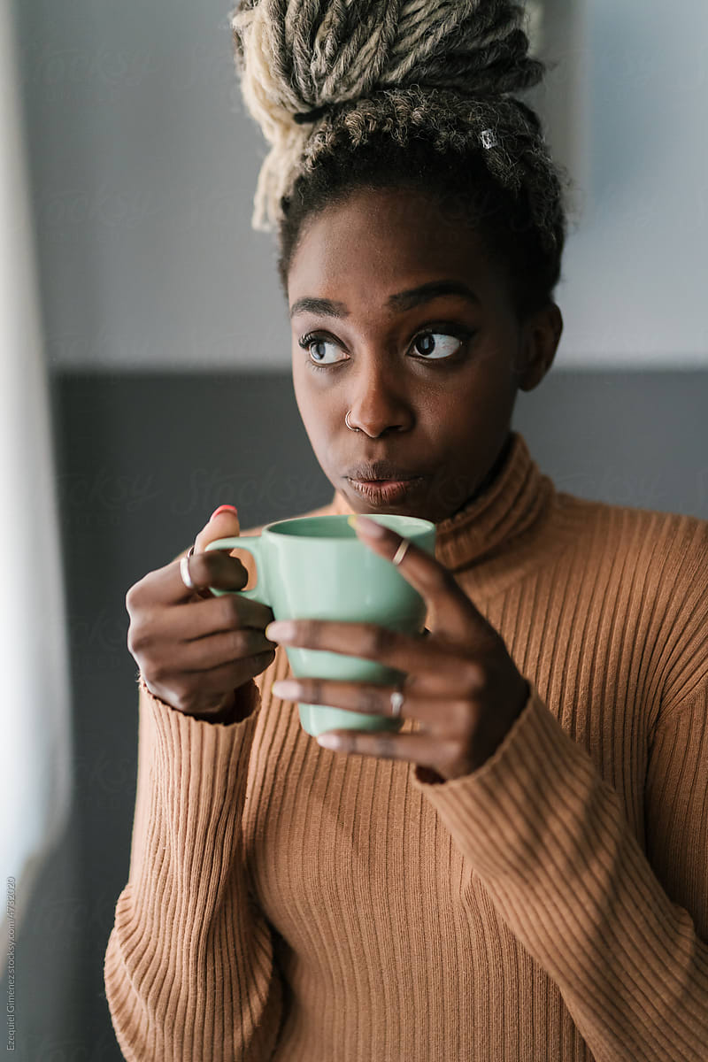 Black woman blowing on hot coffee in mug