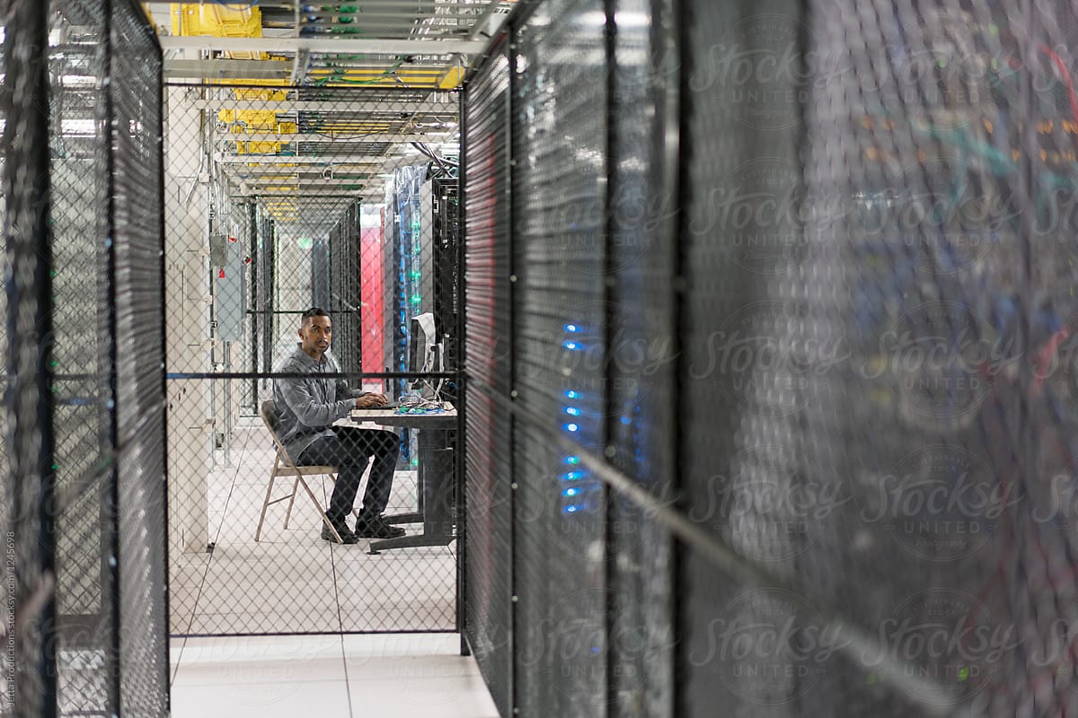 Server room technician sits in a security cage looking at camera