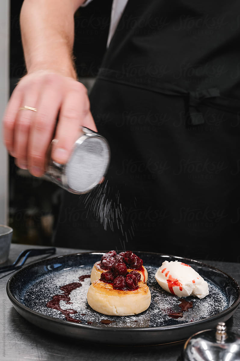 Crop male chef garnishing dessert with powdered sugar