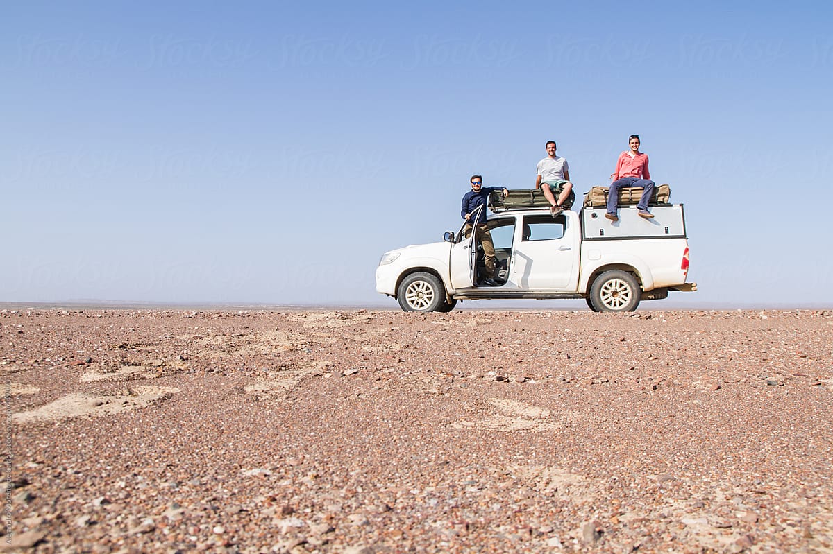 Group of friends on top of a SUV car in the middle of the desert - Adventure travel