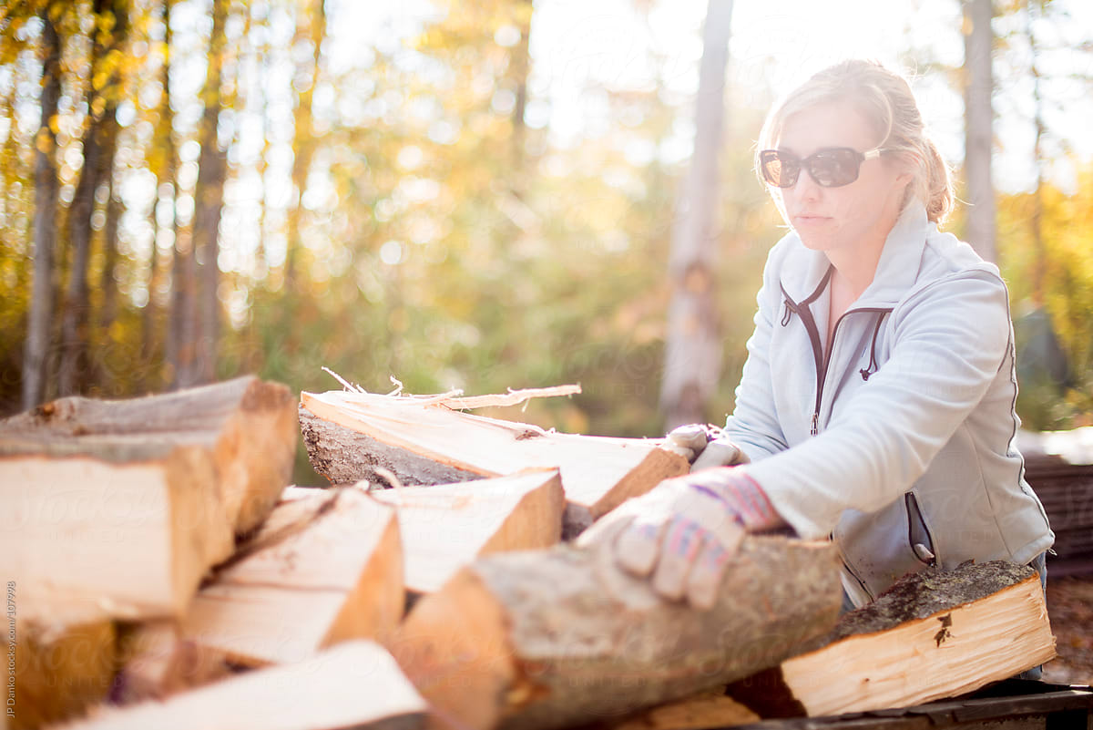 Woman Stacking Hardwood Firewood In Autumn Outdoors at Cottage