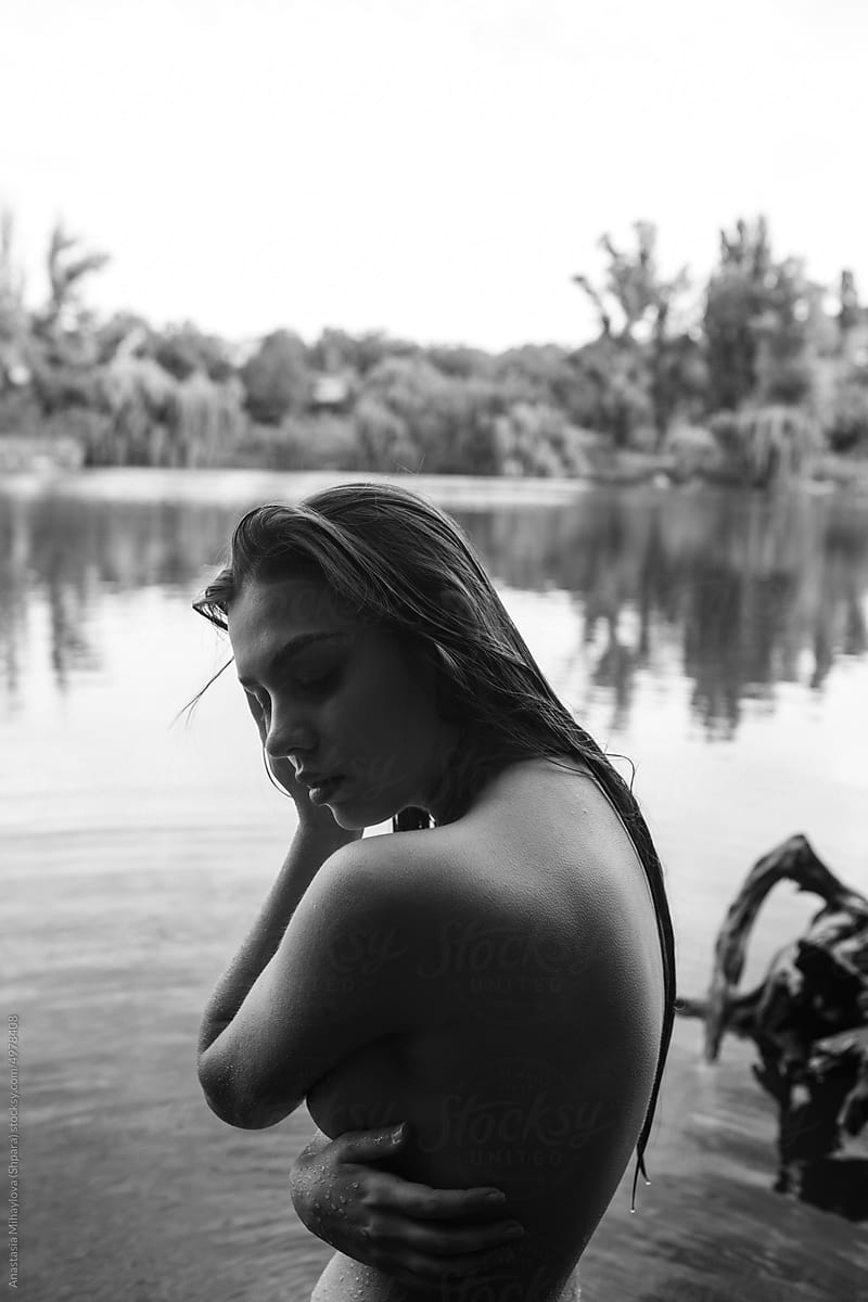 Portrait of naked woman holding her head in water in front of trees