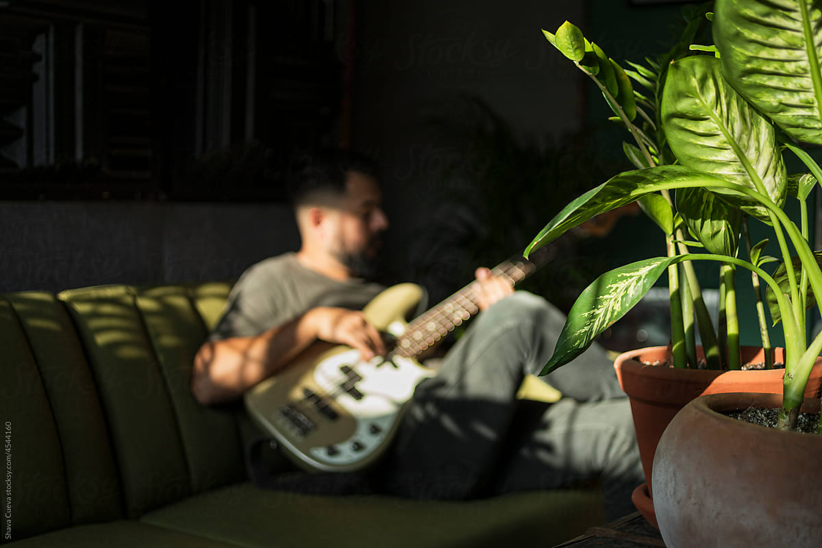 Man sitting on a green couch playing the bass in a room with plants