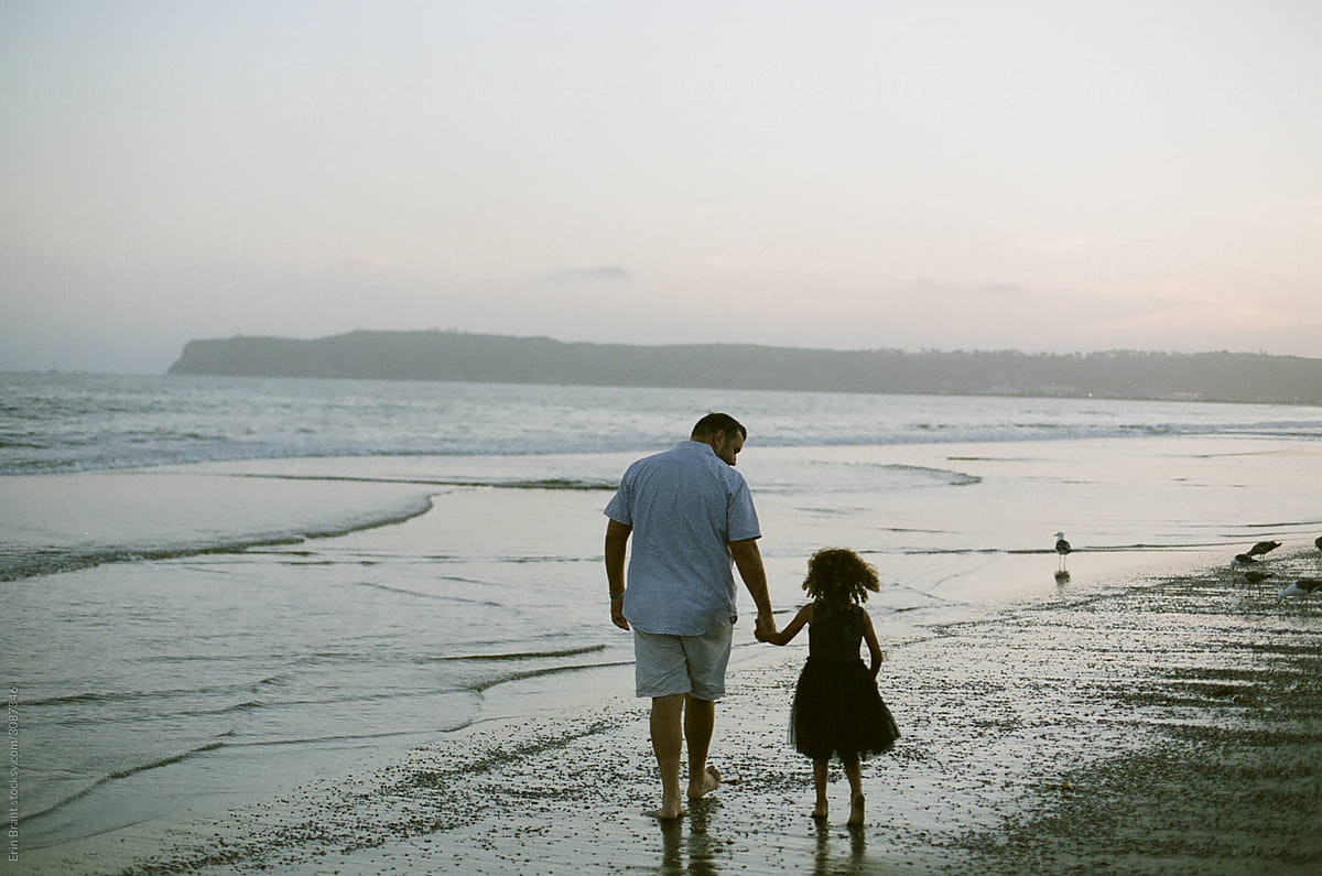 Dad and daughter walking on beach at sunset