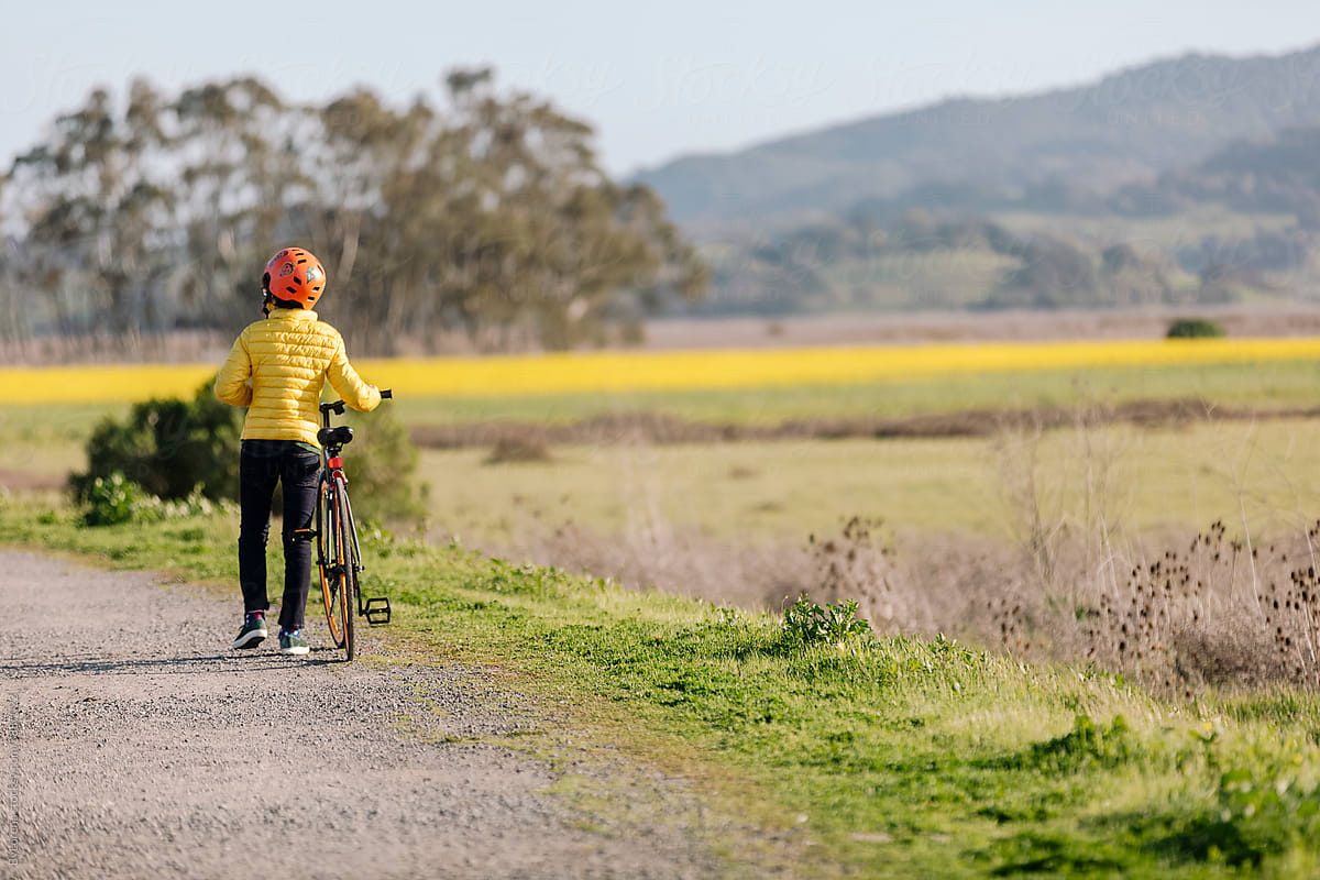 Teenager walking with bike near blooming meadow