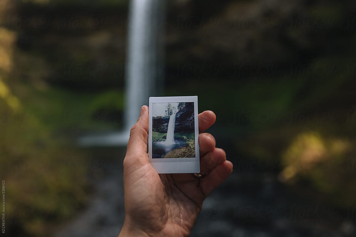 Hand holding a polaroid of a waterfall.