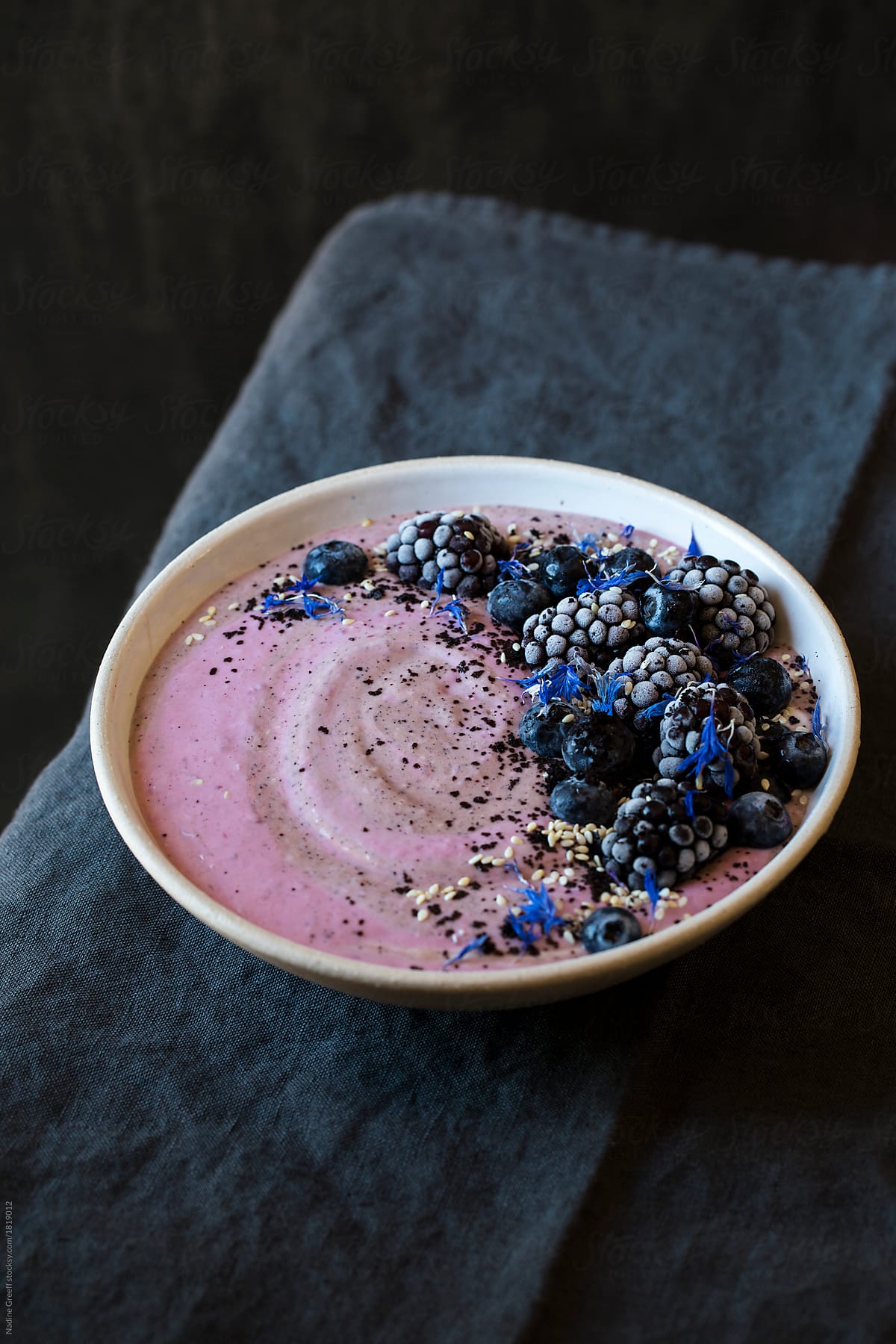 Breakfast smoothie topped with berries, acai berry powder, toasted sesame seeds