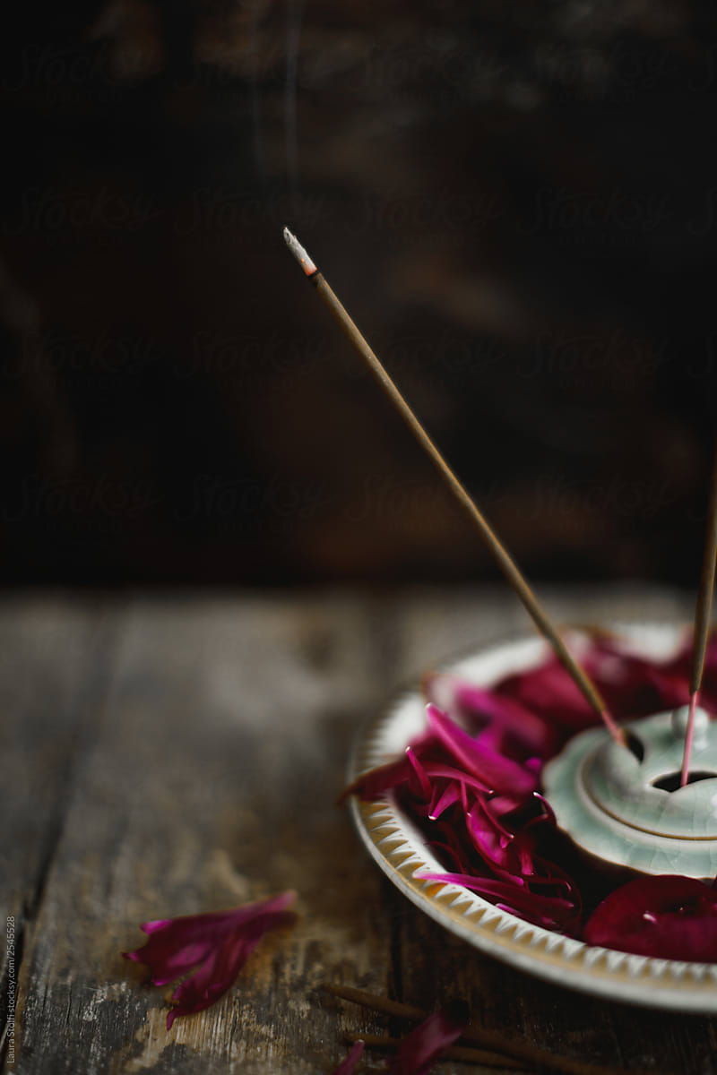 Burning incense stick inside bowl with peonies petals