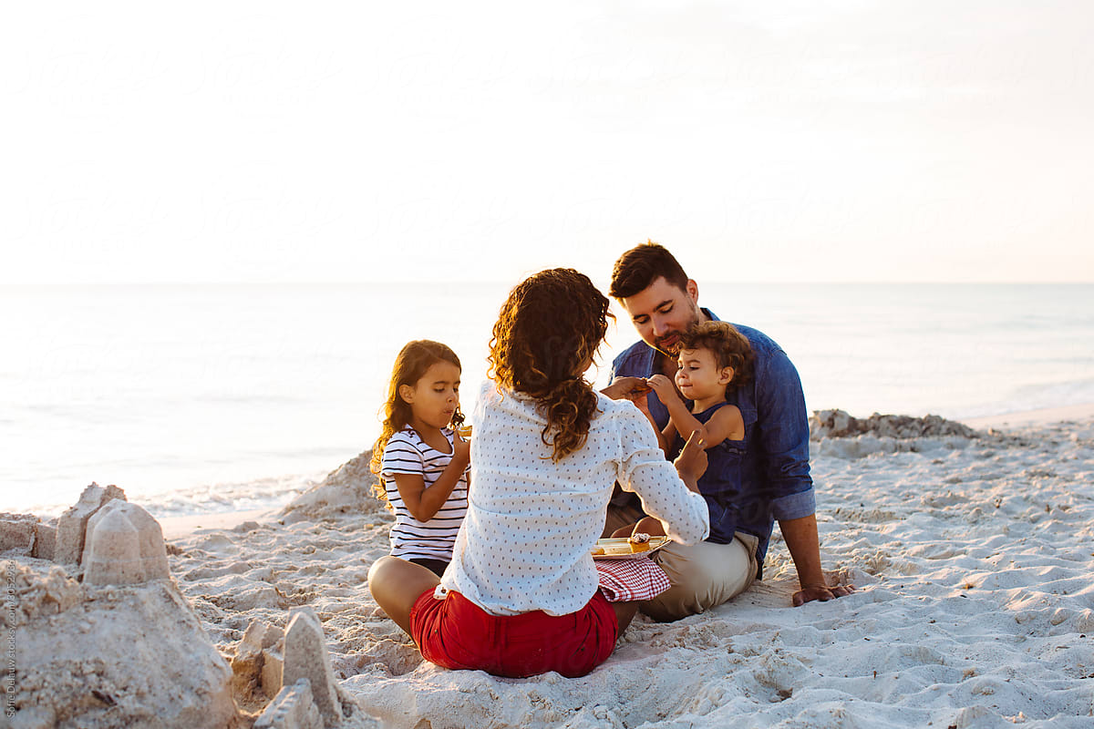 Multiracial family eating snacks on sandy beach