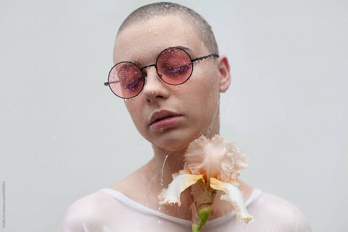 Bald woman with flower stands under water drops
