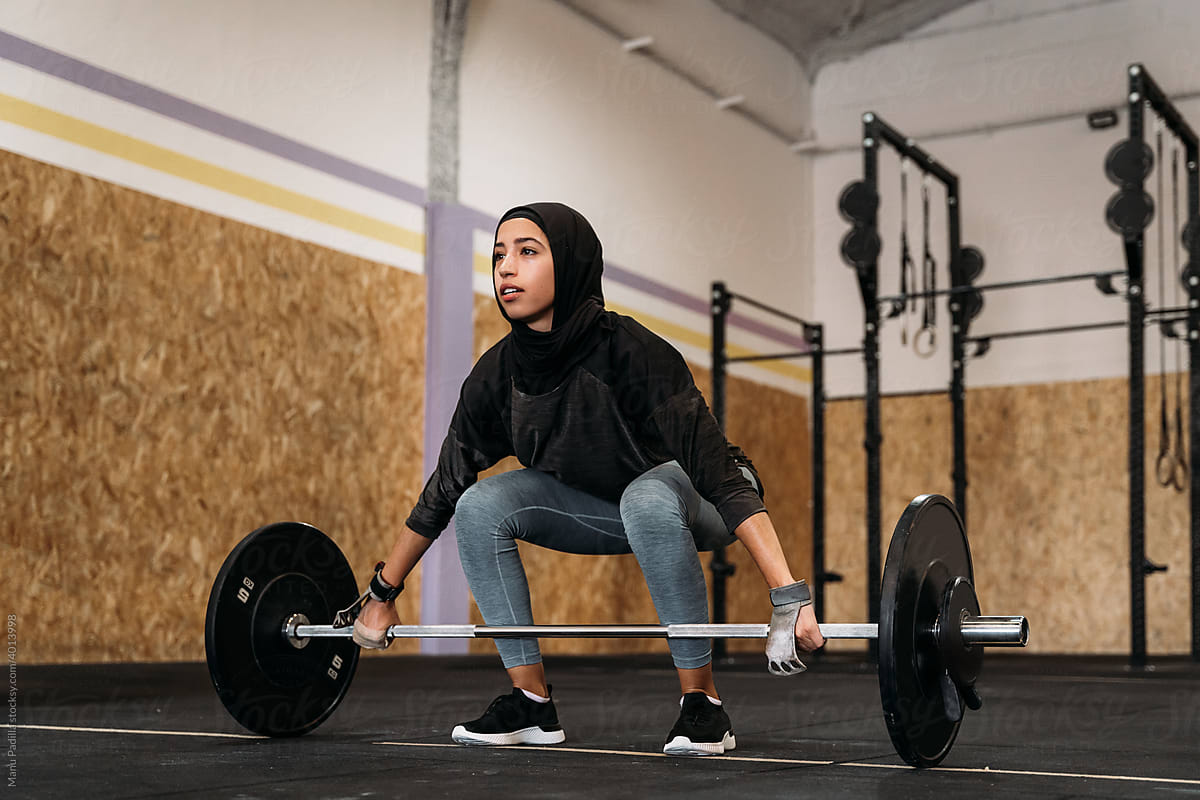Confident Muslim woman lifting barbell in gym