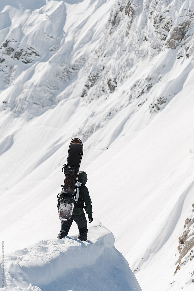Unrecognizable snowboarder walking near snowy mountain