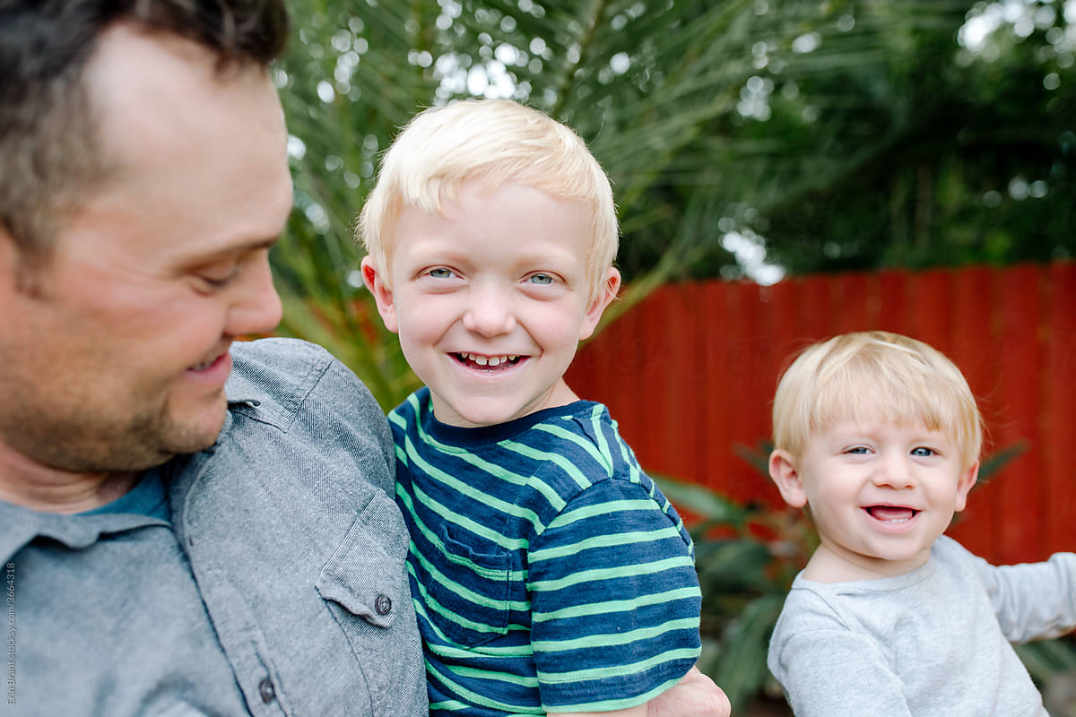 Proud dad with young blue-eyed sons in backyard