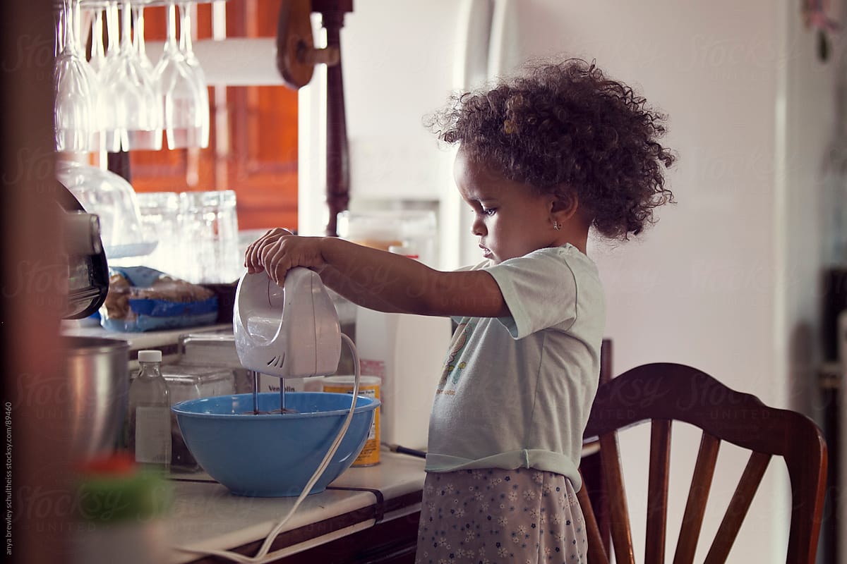Young toddler girl with curly hair using a cake mixer