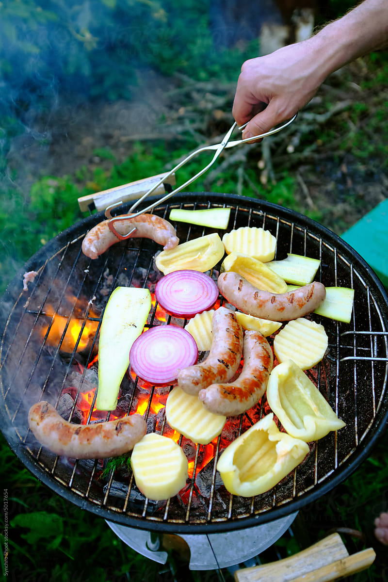 Anonymous person cooking assorted meats and vegetables on the grill