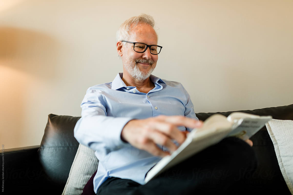 Gray-Haired Man Wearing Glasses Smiles as He Turns the Page in the Book He\'s Reading