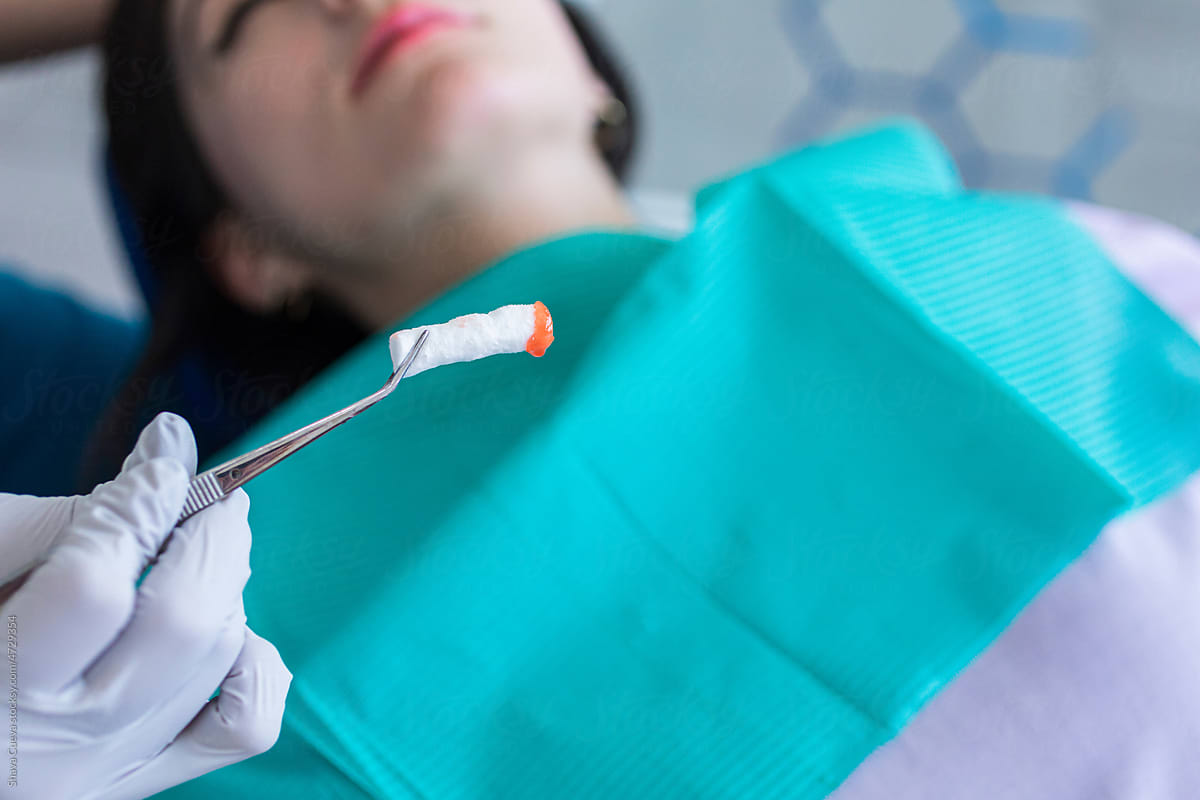 Dentist holding a red anesthetic cotton swab in front of a patient
