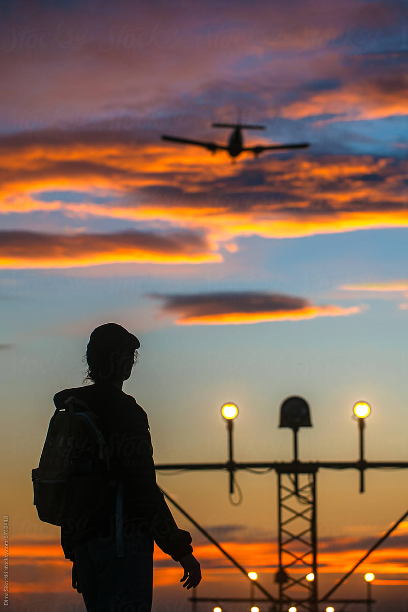 Silhouette of a traveler with a plane and a sunset sky at the airport