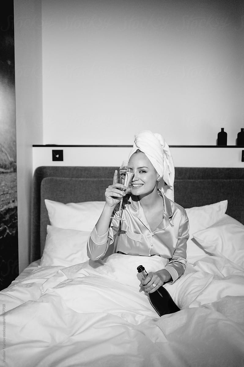 Cheerful female with champagne sitting on hotel bed