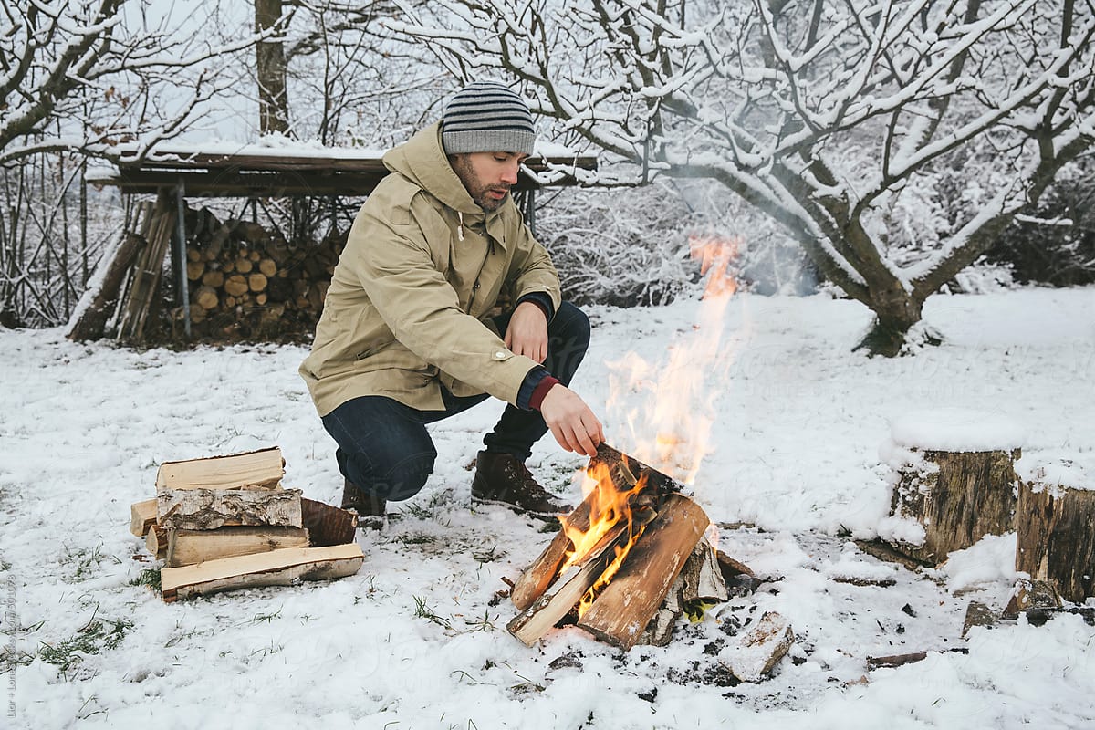 Man adding wood to a bonfire in the snow