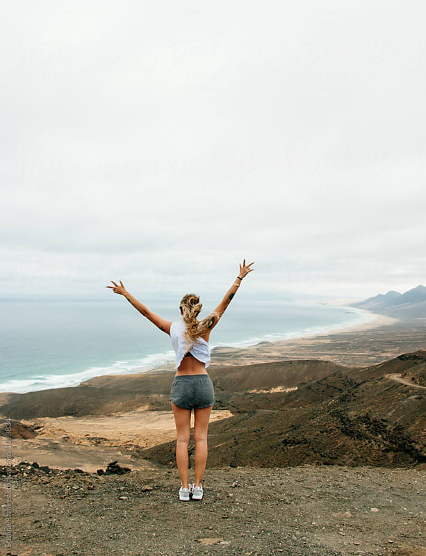Woman raising arms with incredible landscape of mountains and beach