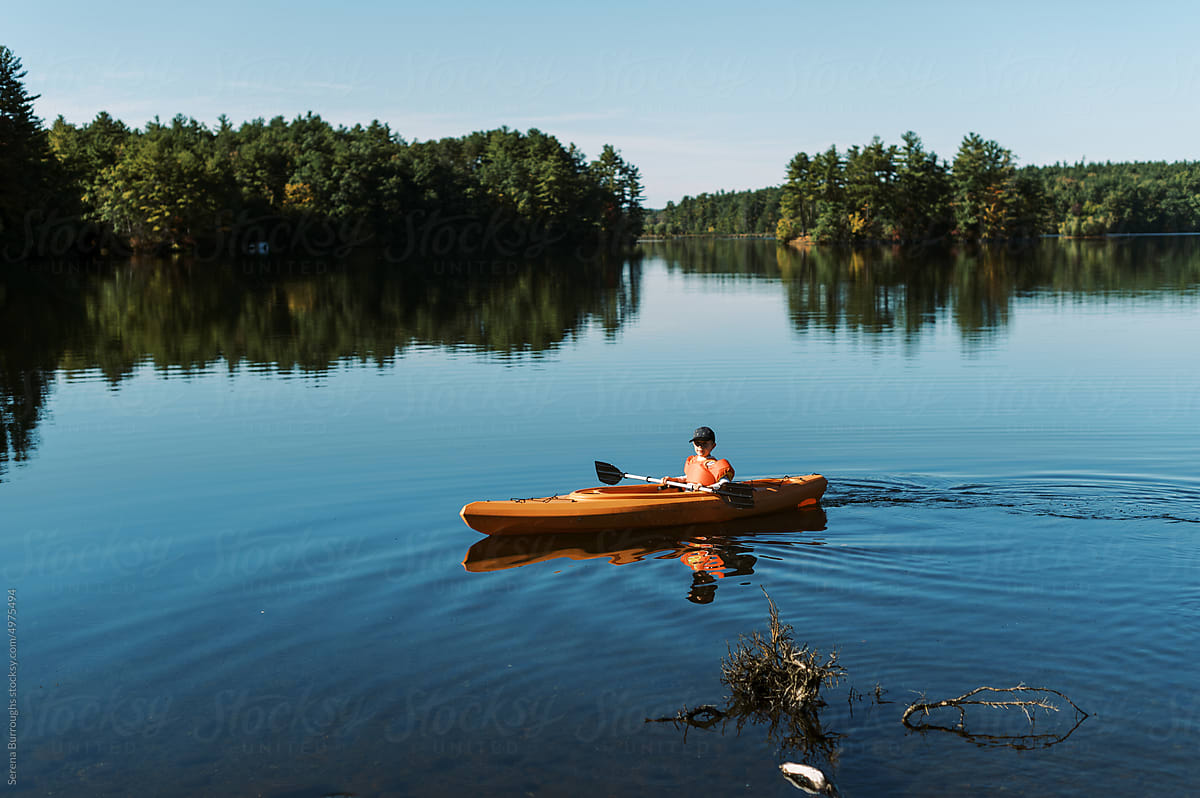Little boy in a kayak alone and paddling independently on a lake