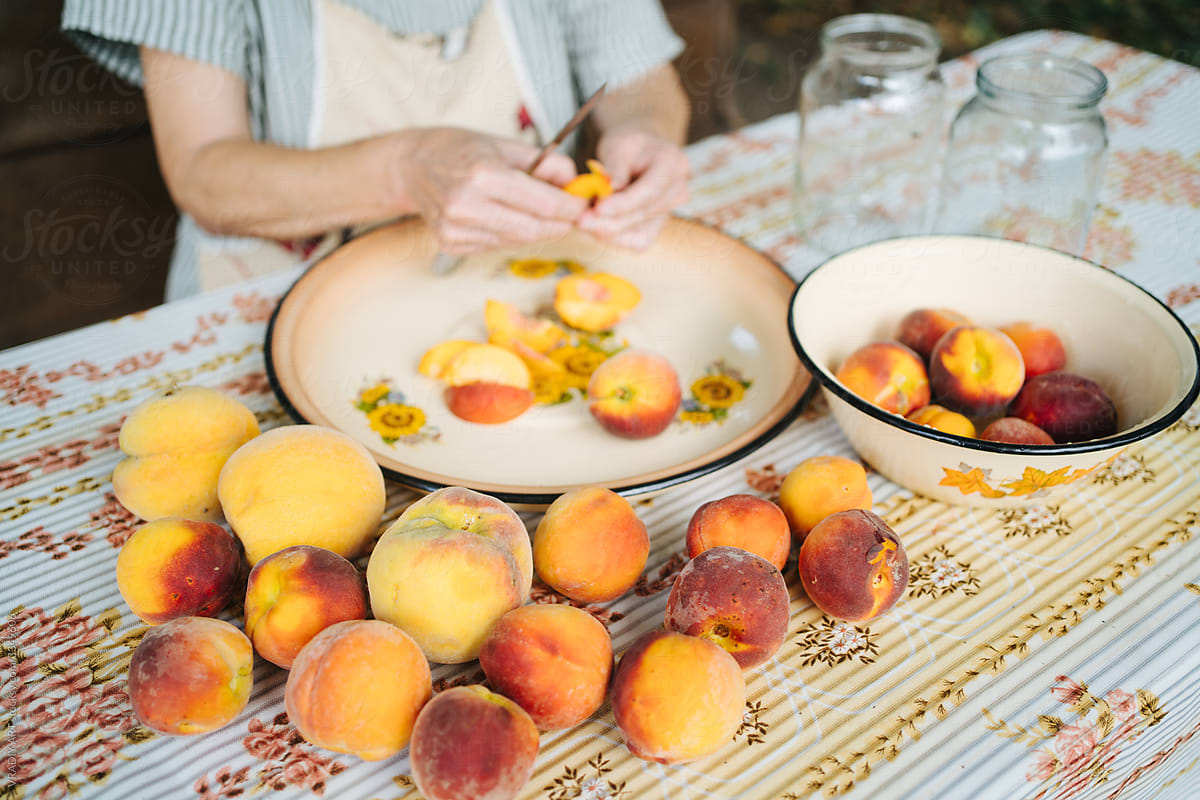 Old woman cutting peaches on table