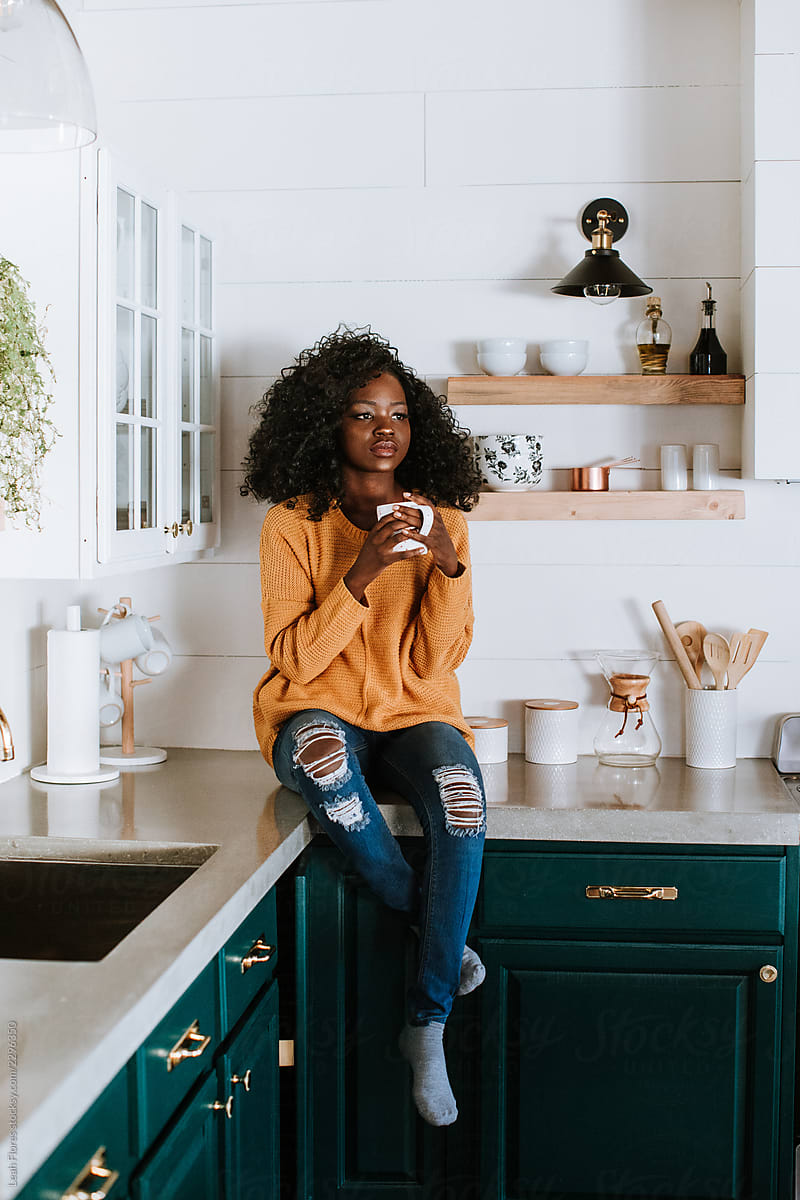 Woman Sitting On Kitchen Counter With Coffee Mug Del Colaborador De