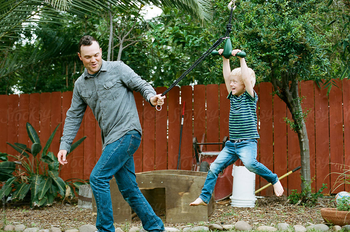 Happy dad pulling young son on backyard zipline.
