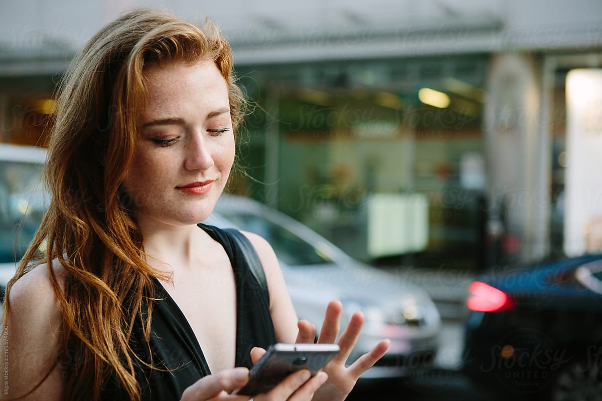 Striking freckled redhead woman looking at her phone in the city