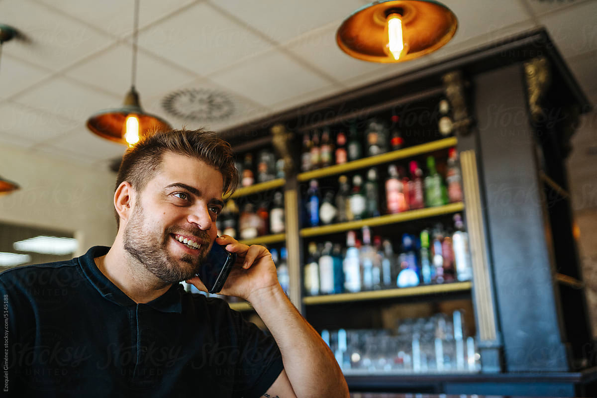 Happy male speaking on smartphone in bar