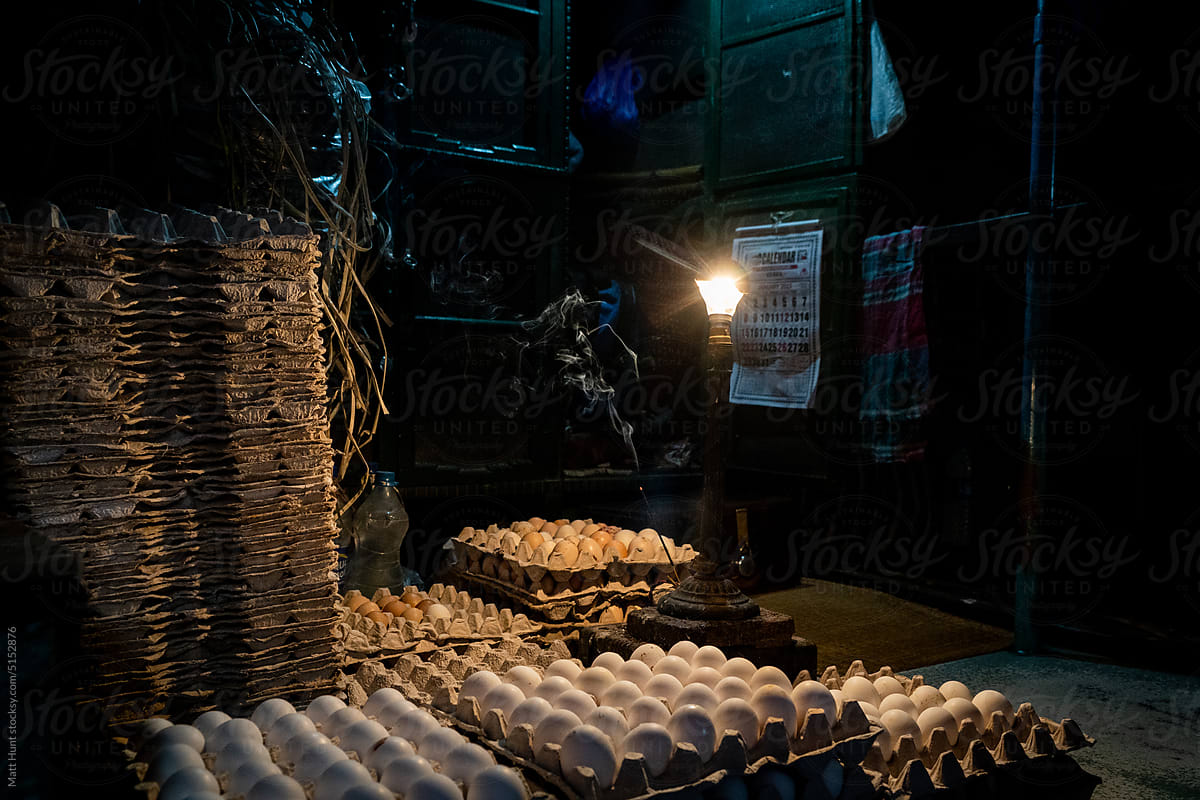 Stacks of eggs in crates illuminated by a single light bulb