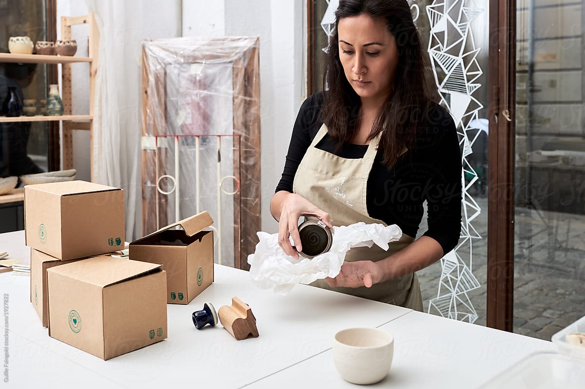 Woman packing crockery into paper in workshop